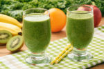 Healthy fresh smoothies with fruits and green kale leaves on wooden background.